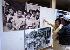 長嶋氏が大学2年生のころ、小学校の同窓生が地元でそろった際に撮影された写真について説明する吉田会長(長嶋氏は前列左、隣の女性は当時の吉田会長)=23日、佐倉市王子台のレイクピアウスイ3階