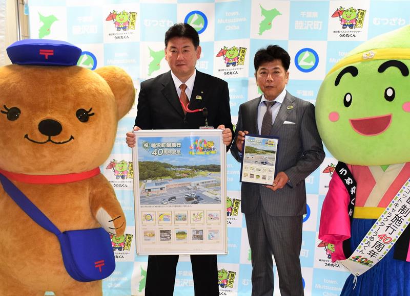 町制施行４０周年の記念切手を持つ田中憲一町長（右）ら＝睦沢町役場