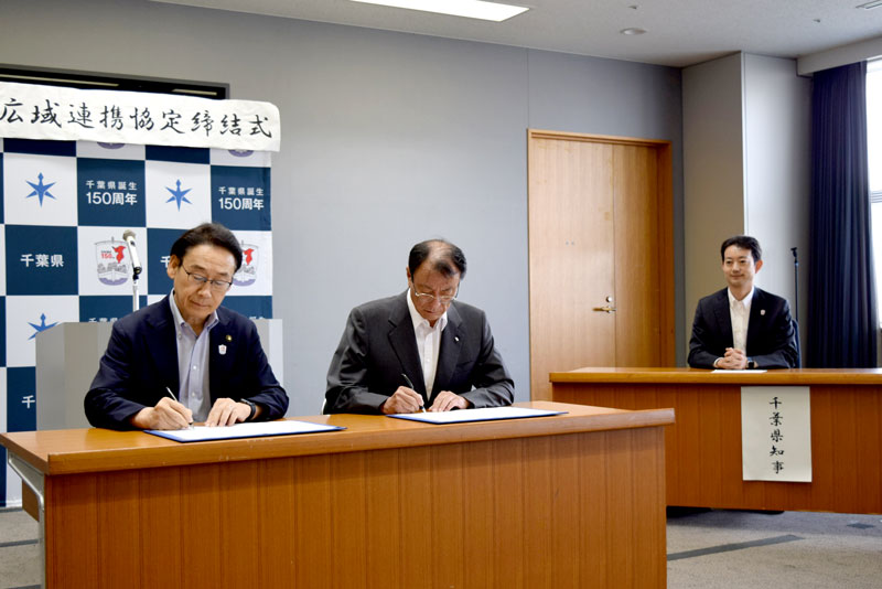 協定書にサインする田中市長(左)と馬淵町長。奥は熊谷知事=28日、千葉県庁