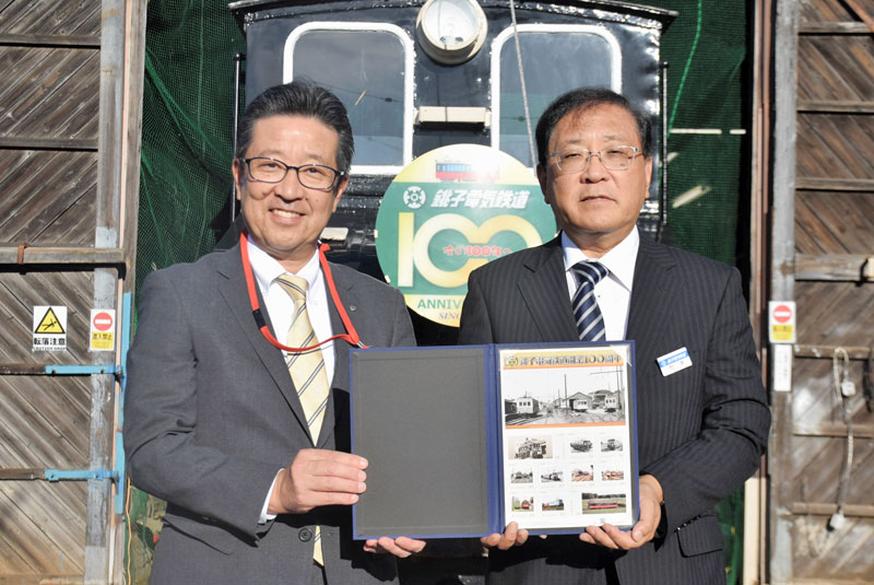 車庫で、銚子電鉄開業１００周年記念のフレーム切手を受け取る銚電の竹本勝紀社長（右）＝銚子市