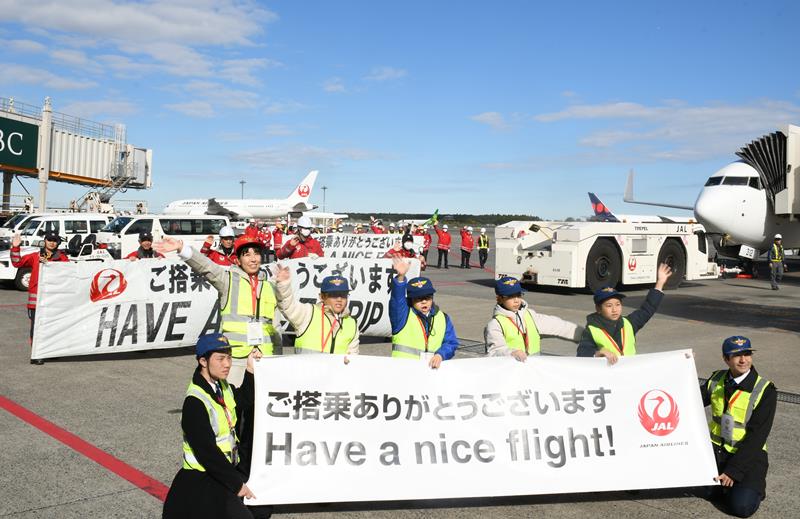 航空機に乗り込む乗客に手を振る小学生やＪＡＬスタッフ＝成田市の成田空港