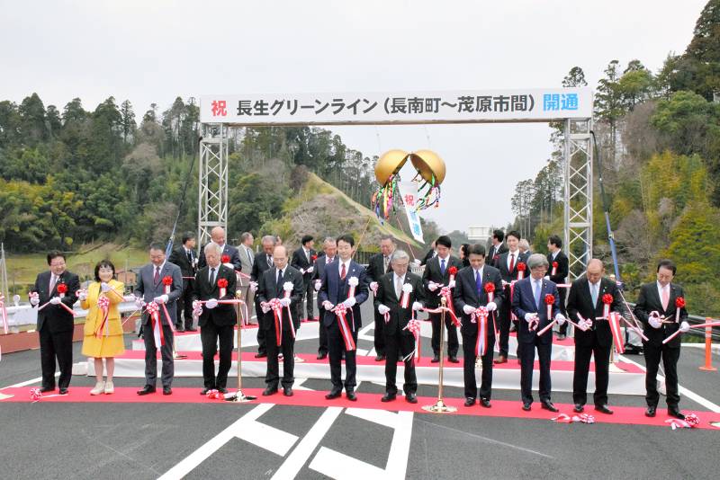 長生グリーンラインの新たな開通区間でテープカットとくす玉割りを行う関係者=24日、茂原市