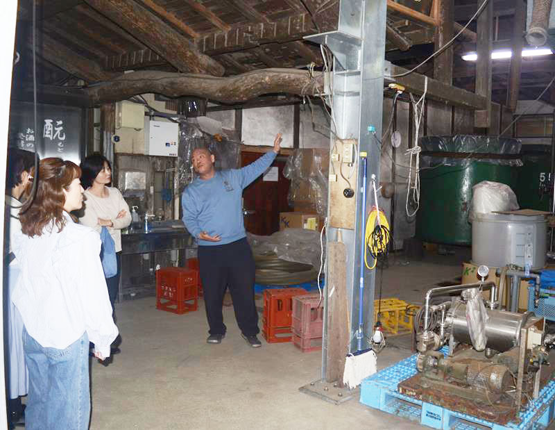 大きなタンクが並ぶ酒蔵の中を案内する守屋雅博さん(中央)=山武市