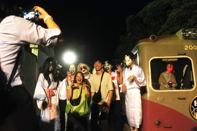 お化け屋敷電車のゾンビや濡女に囲まれ撮影する参加者=銚子電鉄犬吠駅
