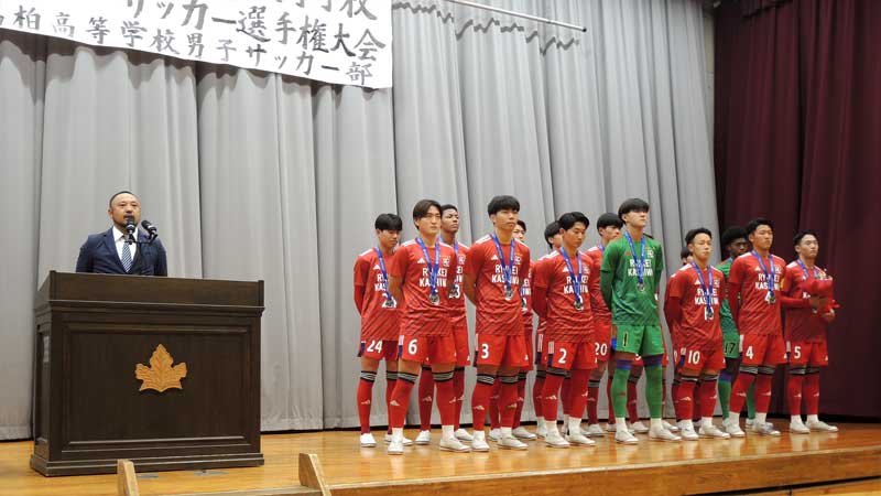 流通経大柏高校で開かれた準優勝報告会でサッカー部員らと並びあいさつする榎本監督=15日、柏市
