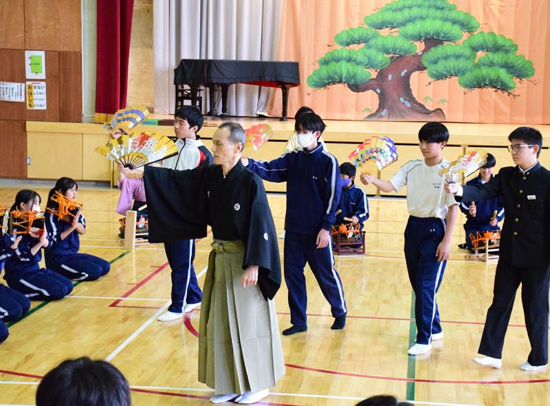 講師の手ほどきを受け、扇を持って舞ったり小鼓をたたいたりする生徒たち＝長柄中