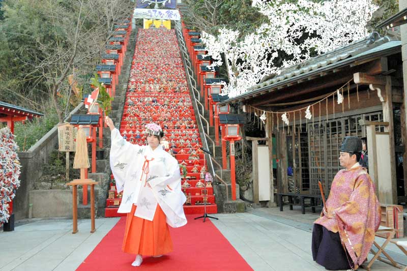 かつうらビッグひな祭りの成功祈願祭で、石段に飾られたひな人形を前に舞を披露する巫女=9日、勝浦市
