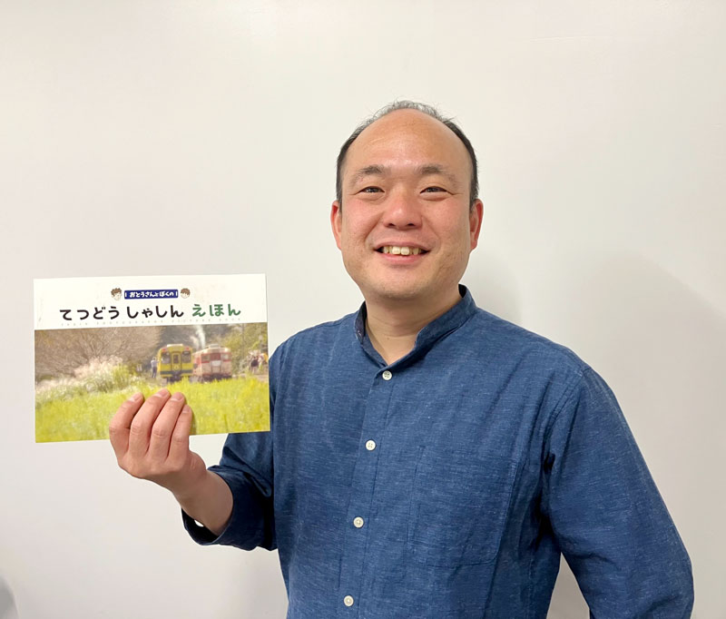 初めて刊行した「おとうさんとぼくのてつどうしゃしんえほん」を手に取る高橋寿太郎さん=2024年12月、横浜市