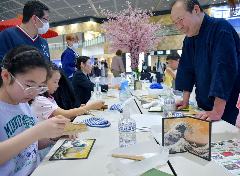 職人に教わりながらミニ屏風を丁寧に作る旅客ら＝成田市の成田空港